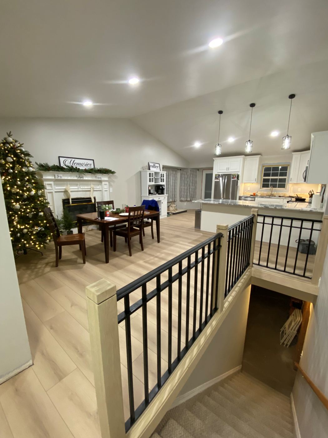 Open living and dining area with new plank flooring and a stair railing, looking through to the remodeled kitchen