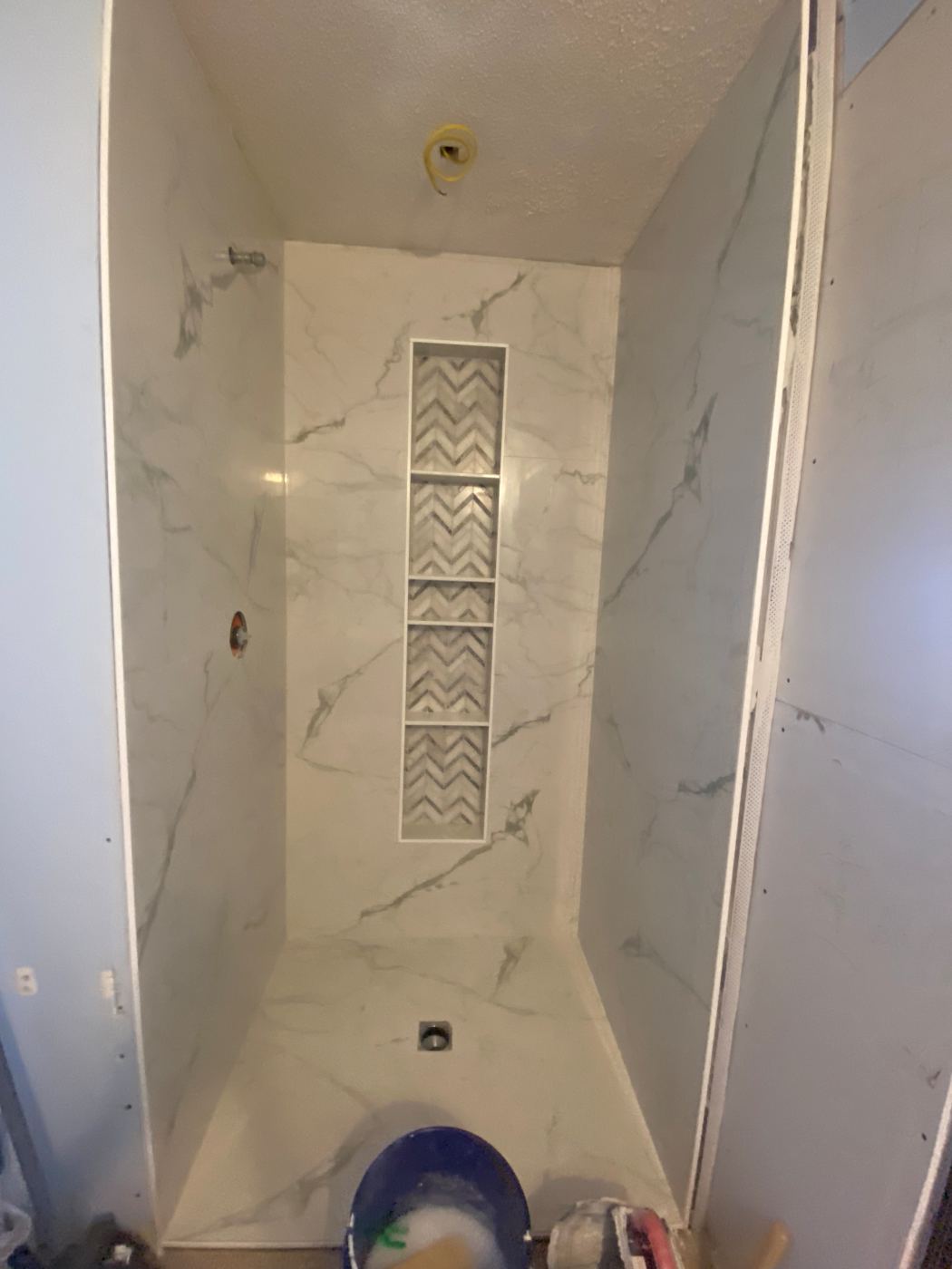 Marble-look shower with a five-shelf herringbone mosaic niche