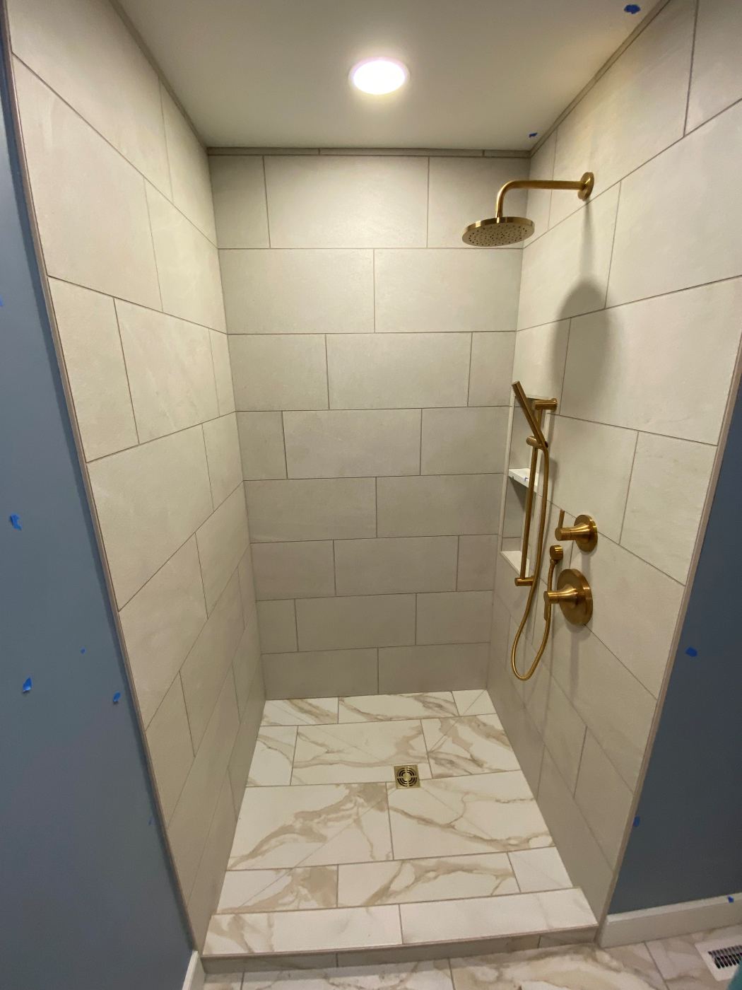 Custom tile shower with brushed brass rain head and a marble tile pan