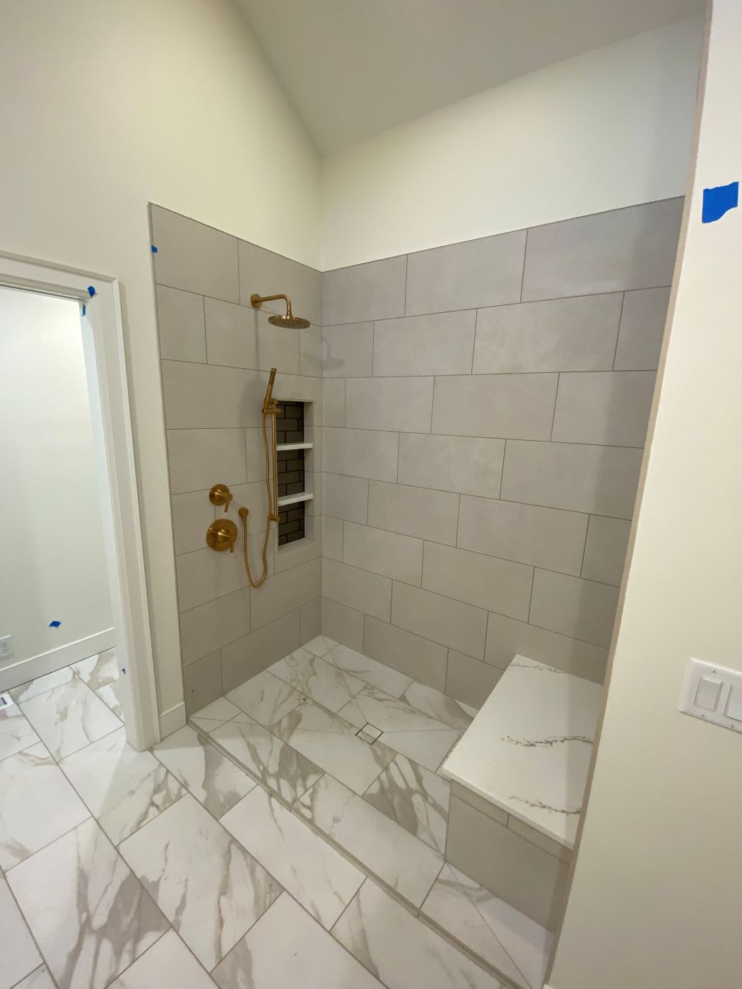 Walk-in shower with brass fixtures and a quartz bench seat