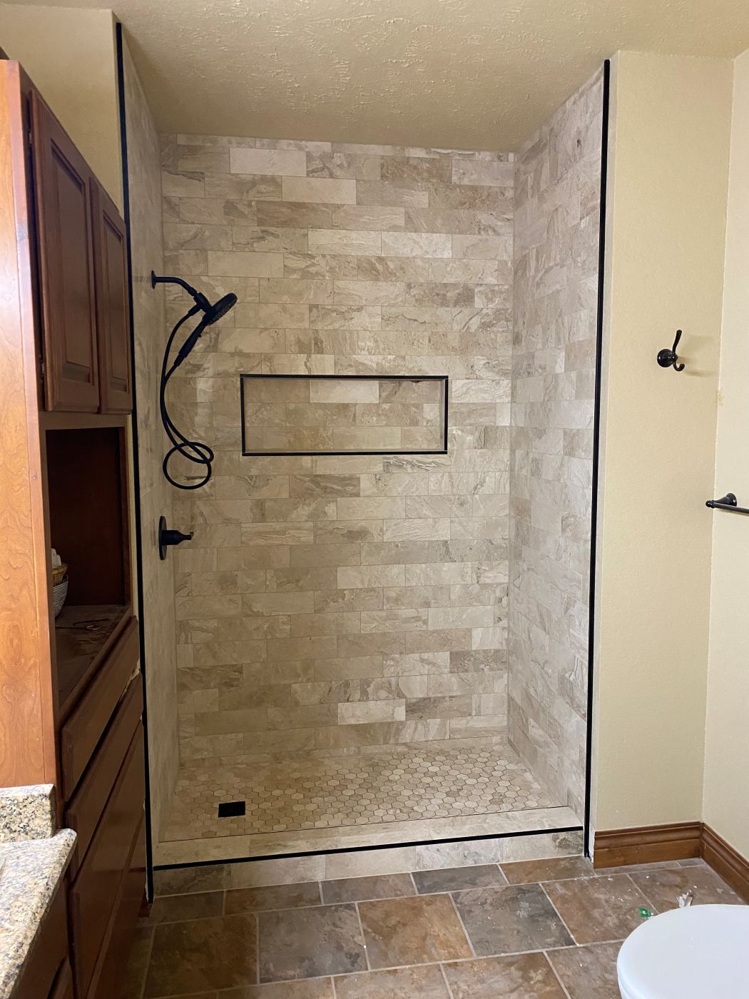 Travertine tile shower with a recessed niche and hex mosaic pan
